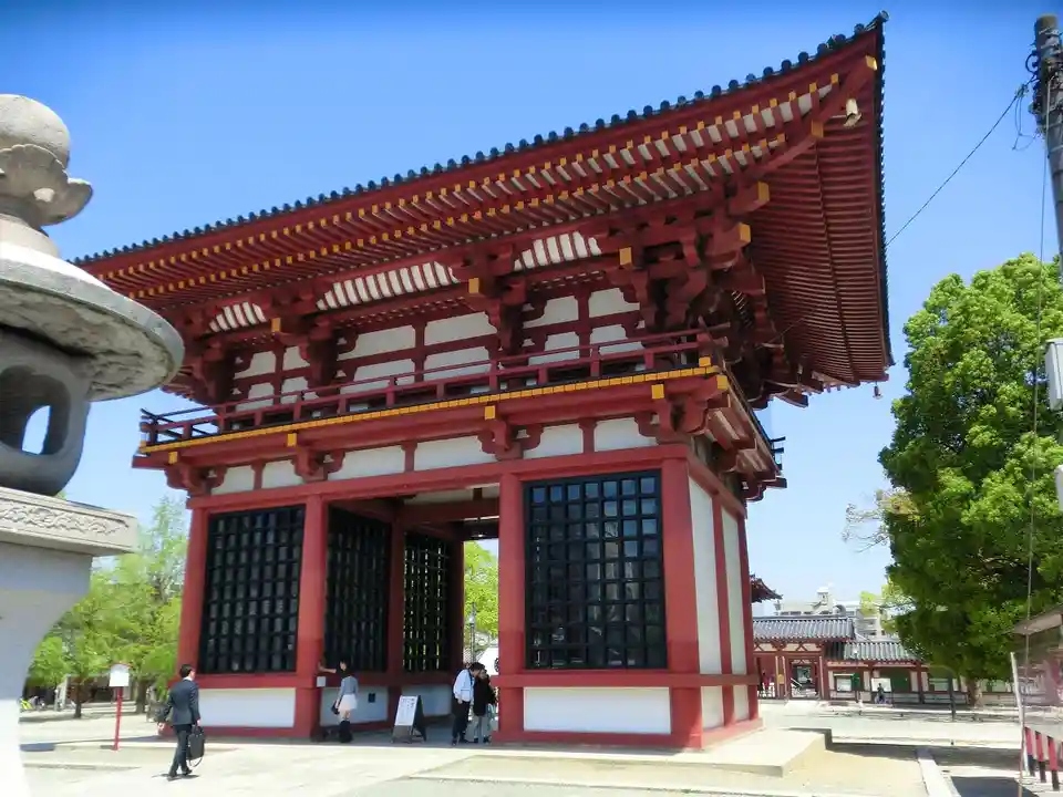 this is a photo of a traditional japanese temple gate with red and white painted wood, black lattice windows, and a curved…