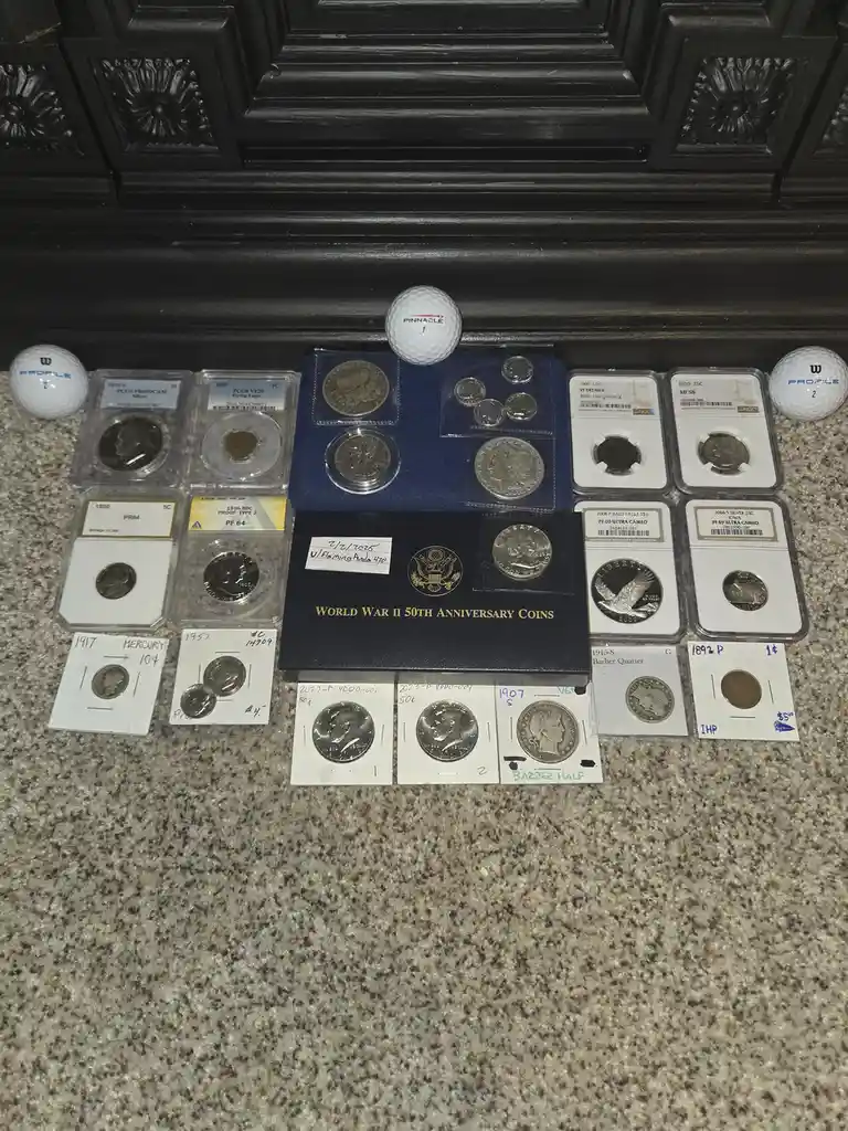 A collection of various graded and ungraded U.S. coins displayed on a carpet, with three golf balls placed strategically…