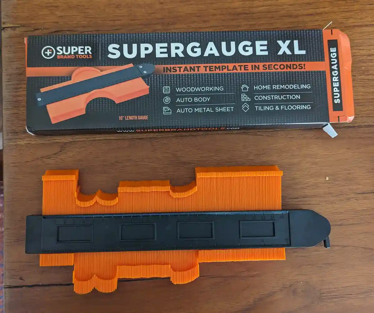 An orange and black 'Supergauge XL' tool sits on a wooden surface next to its packaging, which claims 'instant template in…