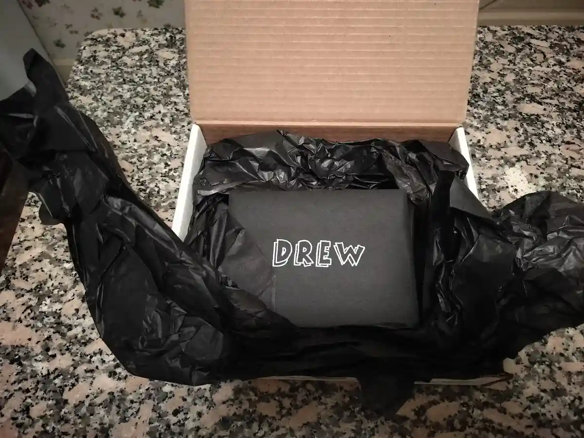 An open cardboard box sits on a speckled granite countertop, filled with crumpled black tissue paper. Nestled inside is a…