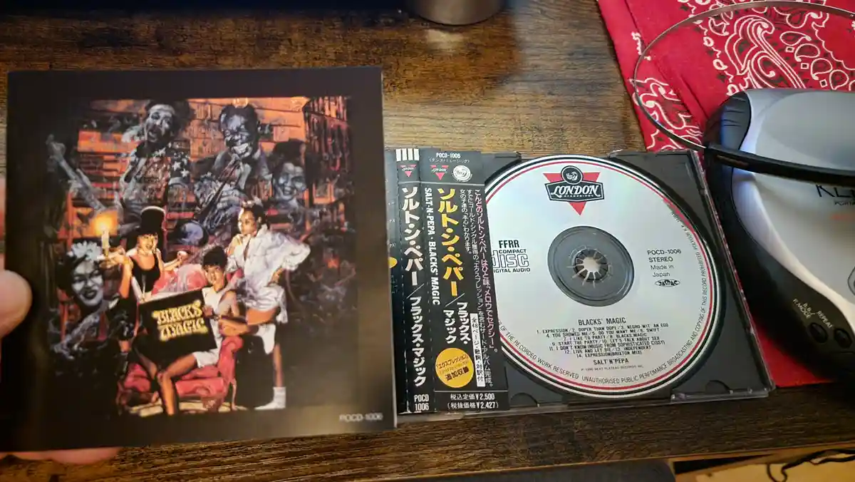 A Japanese CD release of Salt-N-Pepa's 'Blacks' Magic' album is shown open on a wooden table, with the jewel case and disc…