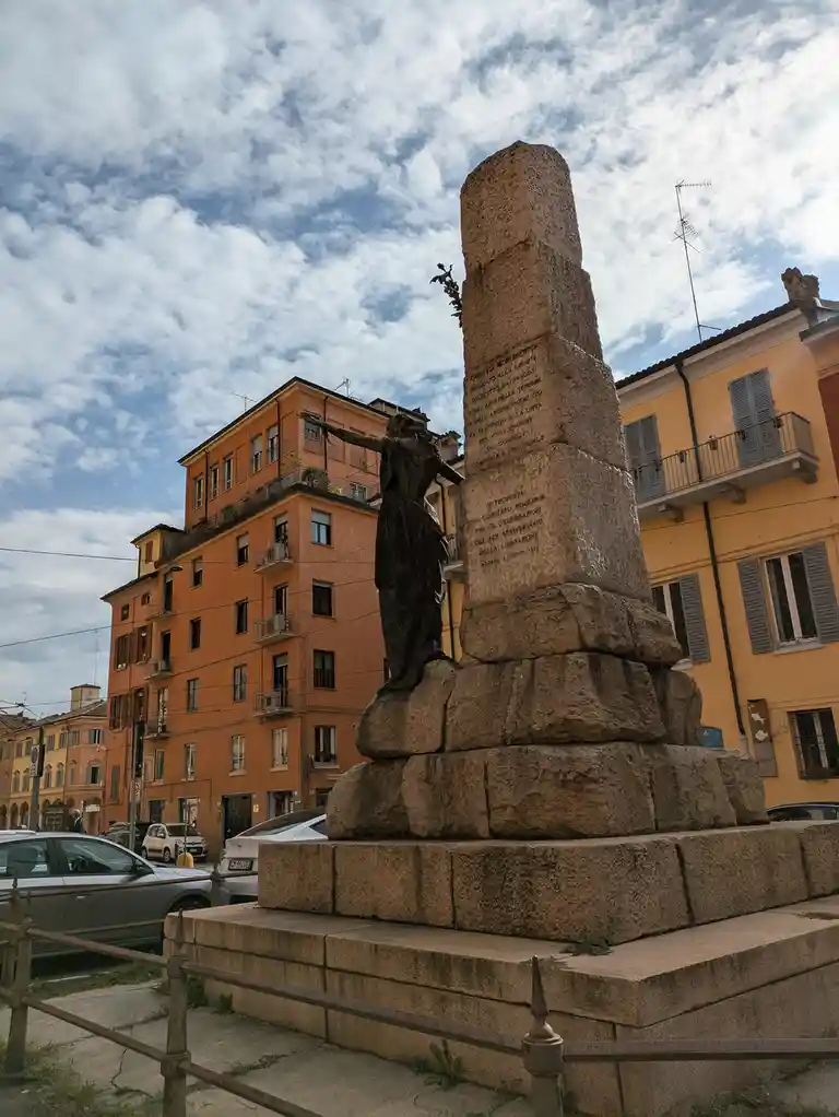 a photograph of a stone monument with a bronze statue of a woman with outstretched arms, set in an urban square with…