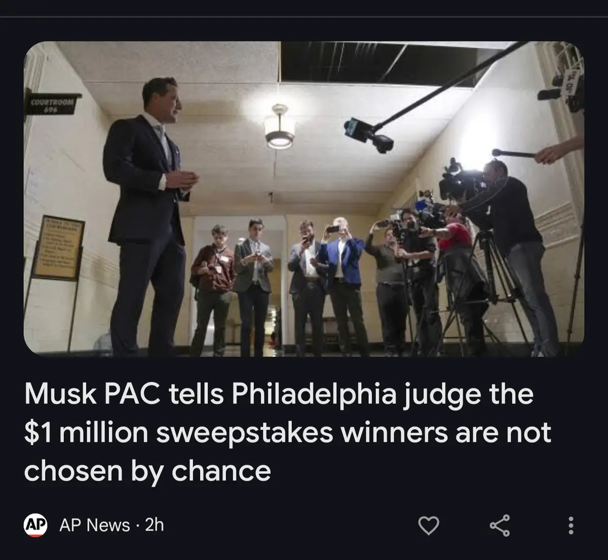 A man in a dark suit stands in a hallway labeled 'COURTROOM 696' addressing a group of reporters and cameramen. The overlaid…