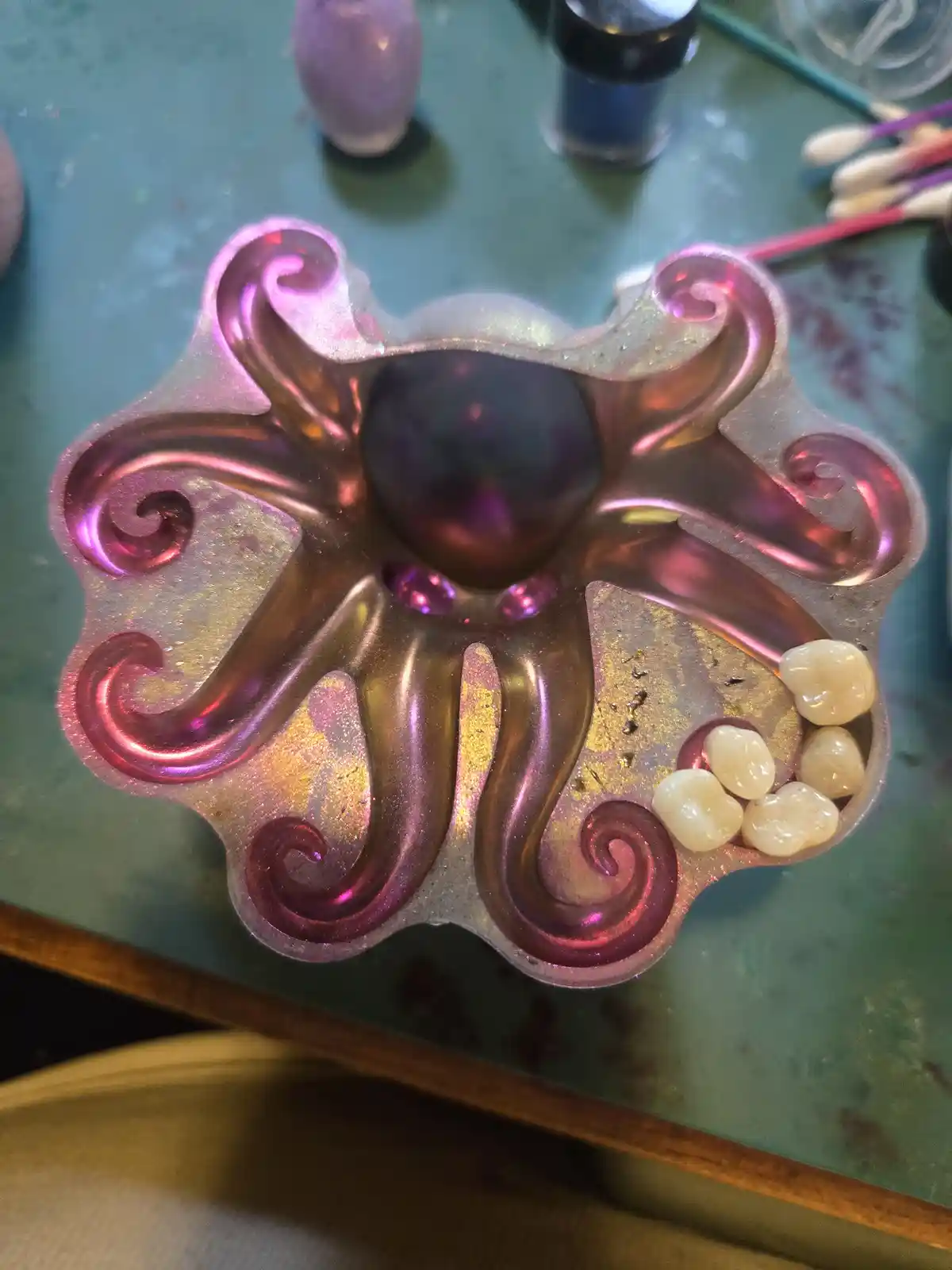 A shiny, iridescent octopus-shaped mold with swirling tentacles sits on a green work surface, holding several small…