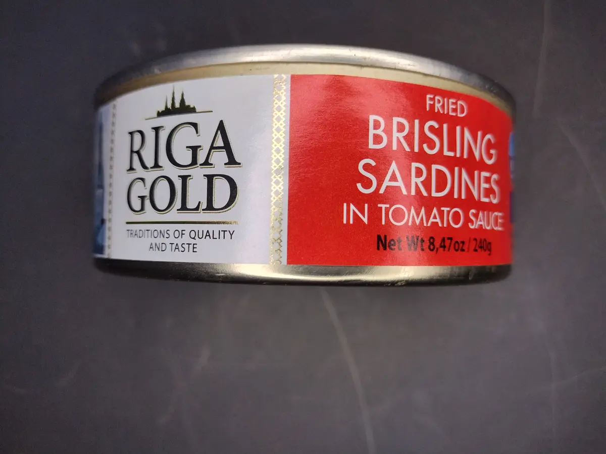 A close-up of a Riga Gold canned food label showing 'FRIED BRISLING SARDINES IN TOMATO SAUCE' in bold white text on a red…