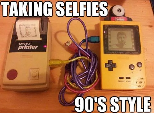 A yellow Game Boy Color sits next to a beige Game Boy Printer on a wooden surface, connected by a tangle of colorful cables…