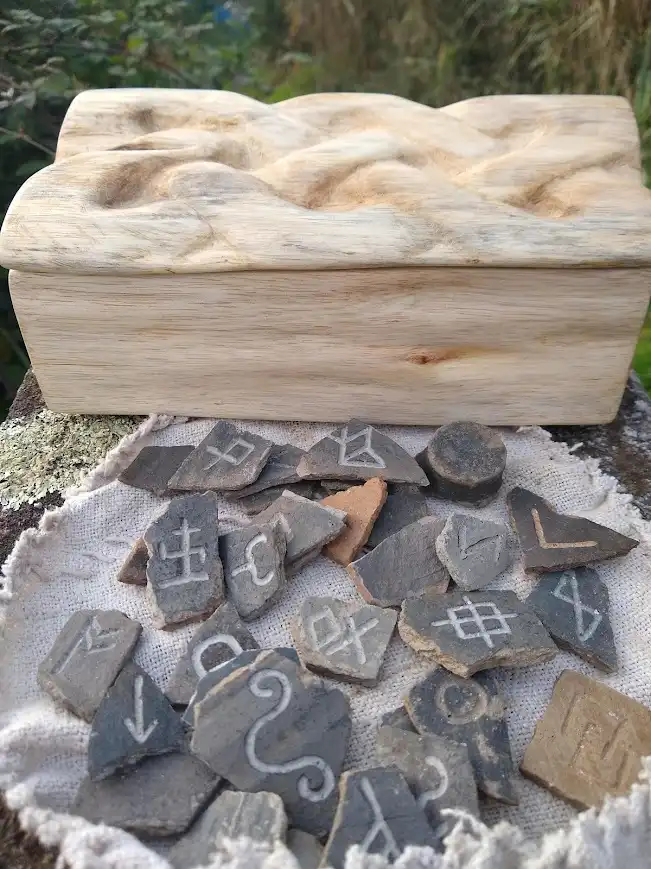 A wooden box with a carved lid sits behind a pile of broken, irregularly shaped stone fragments, each engraved with various…