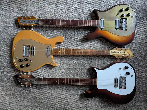 Three Rickenbacker electric guitars are laid out horizontally on a textured gray carpet, showcasing different body finishes…