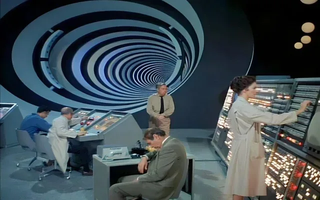 A scene from a 1960s sci-fi TV show shows five people in a futuristic control room with a large, hypnotic spiral tunnel…