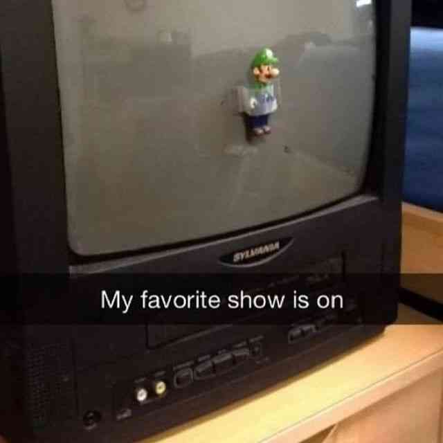 A small green-clad Mario figurine is stuck to the dusty screen of an old, black, boxy CRT television. The TV, branded…