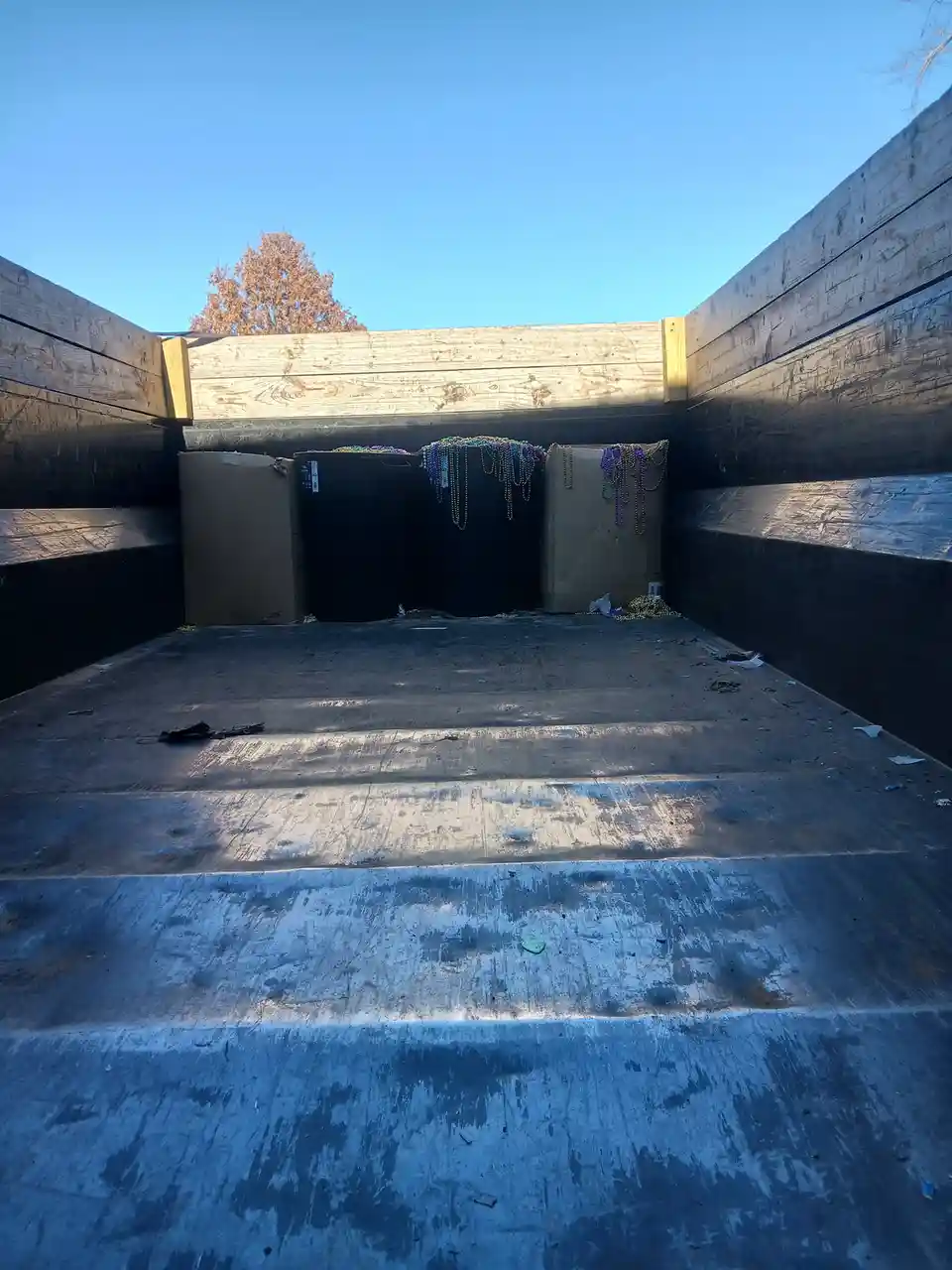 A low-angle shot of the inside of a large dumpster with wooden walls, showing cardboard boxes and a black trash can at the…