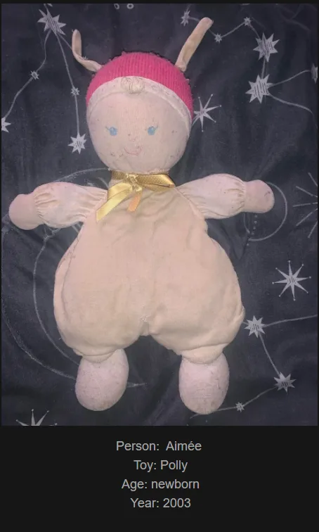 A vintage, beige plush doll with a pink knitted hat and small antlers lies on a dark fabric with star and constellation…