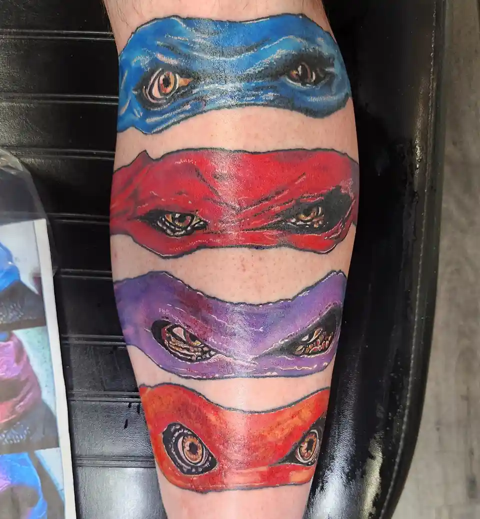 A close-up photo shows a tattoo on a person's leg featuring the eyes of the four Teenage Mutant Ninja Turtles, each with…