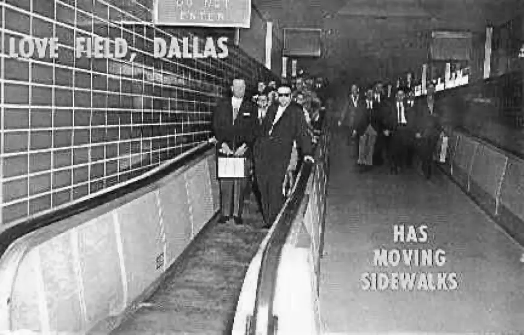 A black-and-white photo shows people walking on a moving sidewalk inside Love Field, Dallas, with large text overlaid on the…