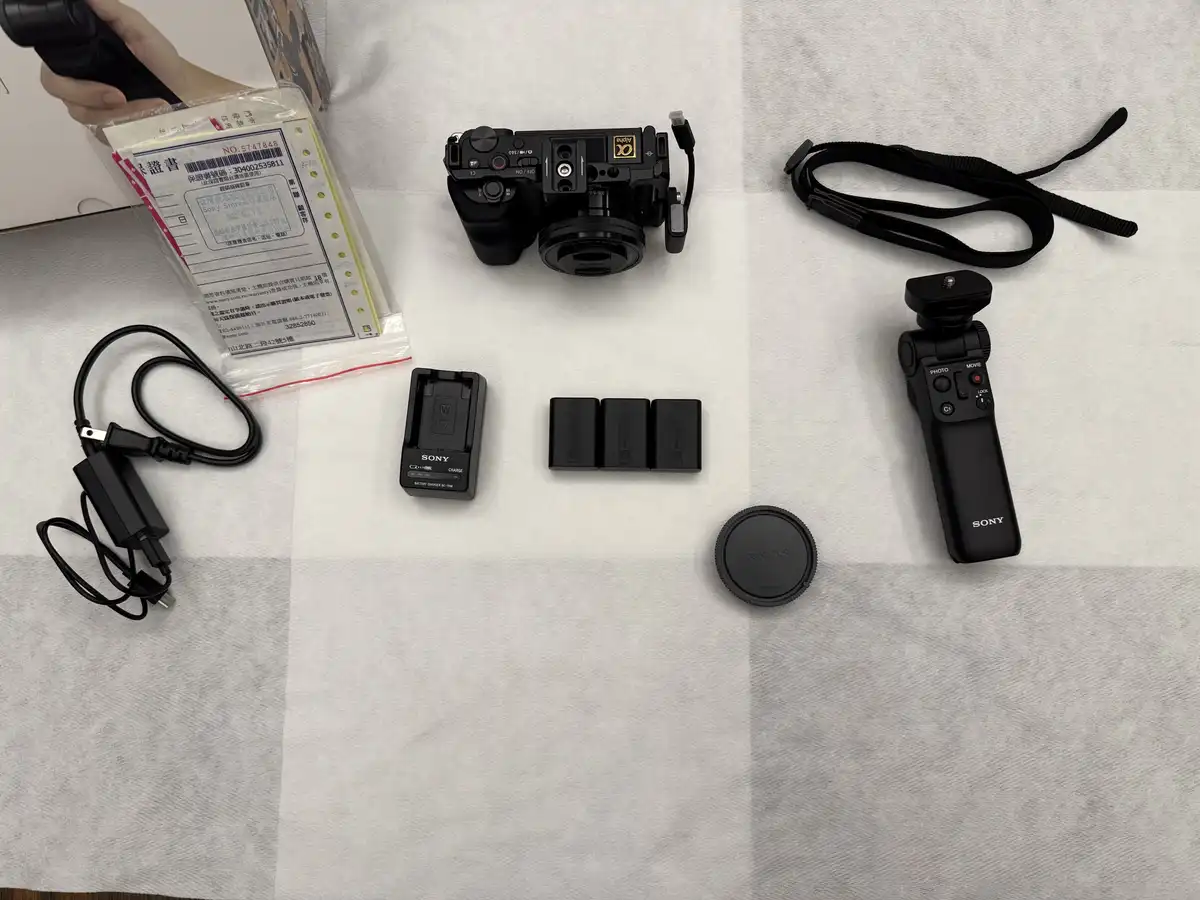 An overhead shot displays a Sony camera and its accessories laid out on a white towel, including a battery charger, three…