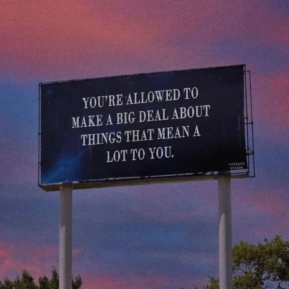 A large outdoor billboard with white text on a dark background stands against a twilight sky with pink and purple clouds…