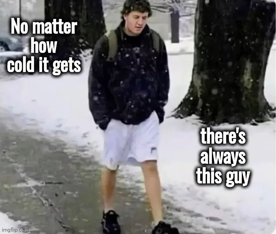 A young man stands outdoors in snowy weather, wearing a dark jacket, white shorts, and dark shoes with a backpack. Snow is…