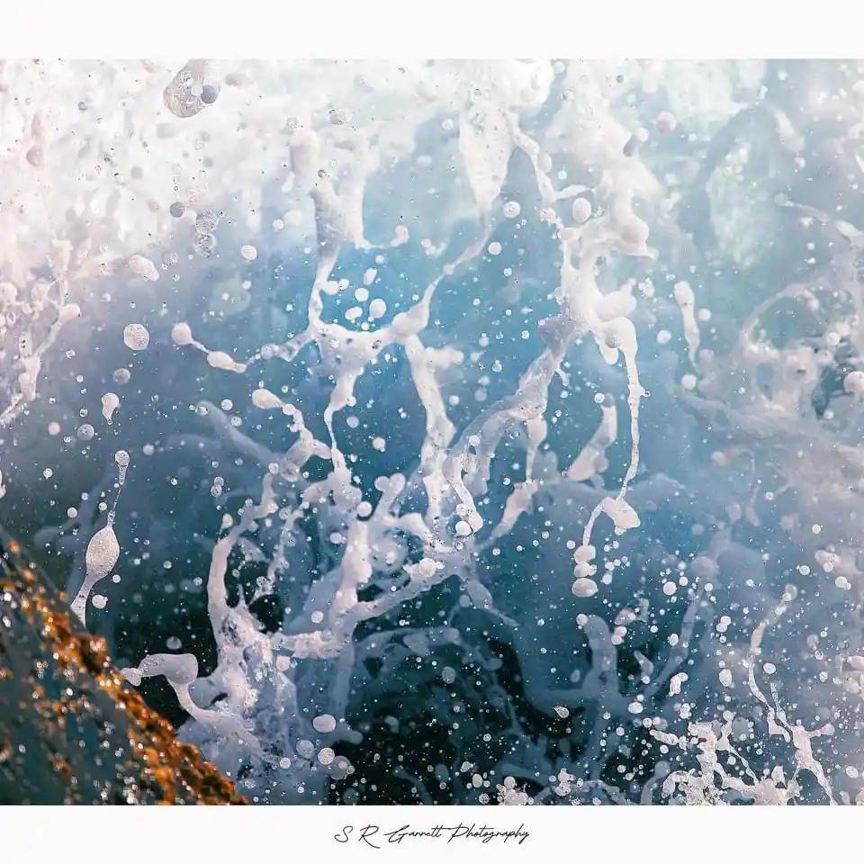 A close-up photograph captures a dynamic splash of ocean water, with white foam and droplets suspended in mid-air against a…
