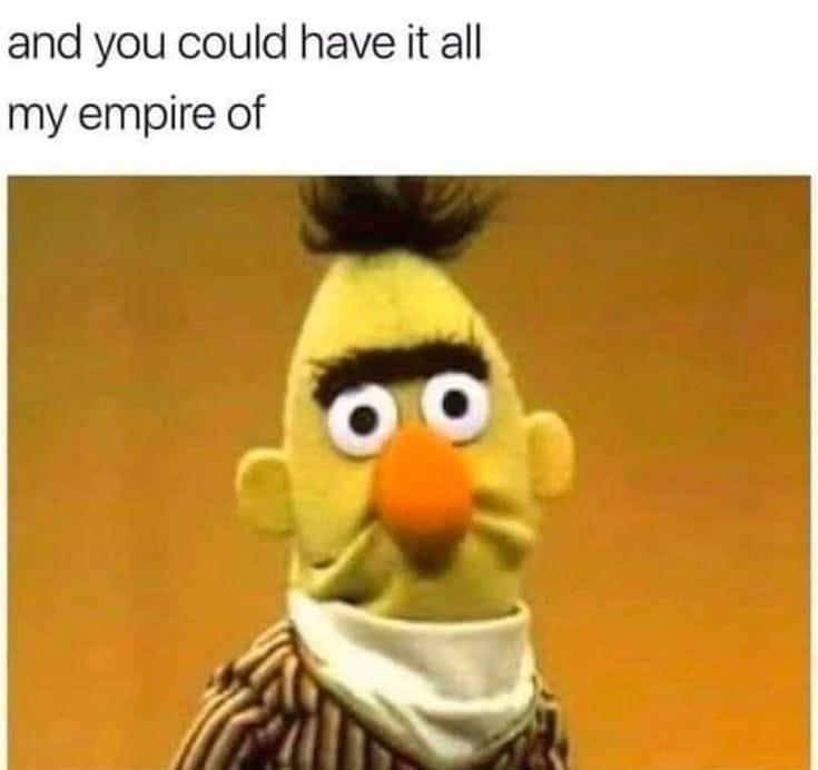 A close-up image of the Muppet character Bert, who has a yellow face, orange nose, black eyebrows, and a tuft of black hair…