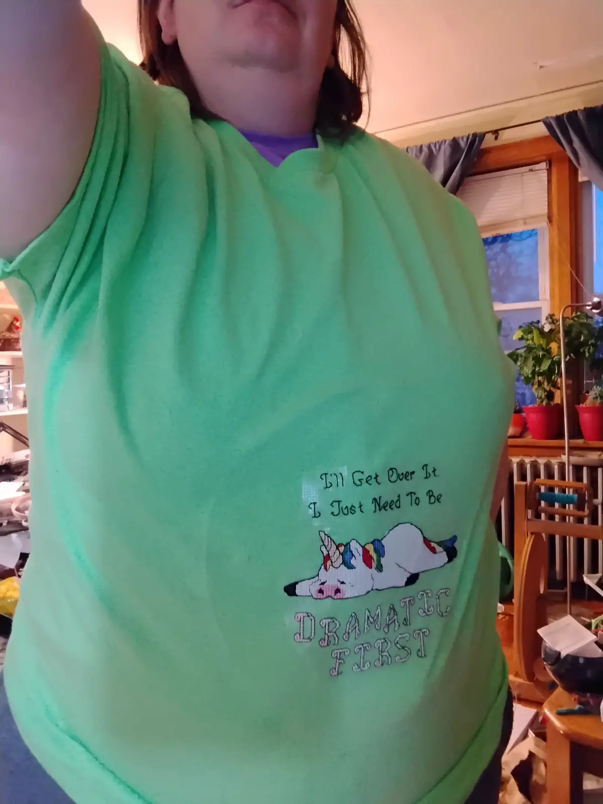 A person wearing a bright green t-shirt with a cross-stitched design featuring a sleeping unicorn and the text 'I'll Get…