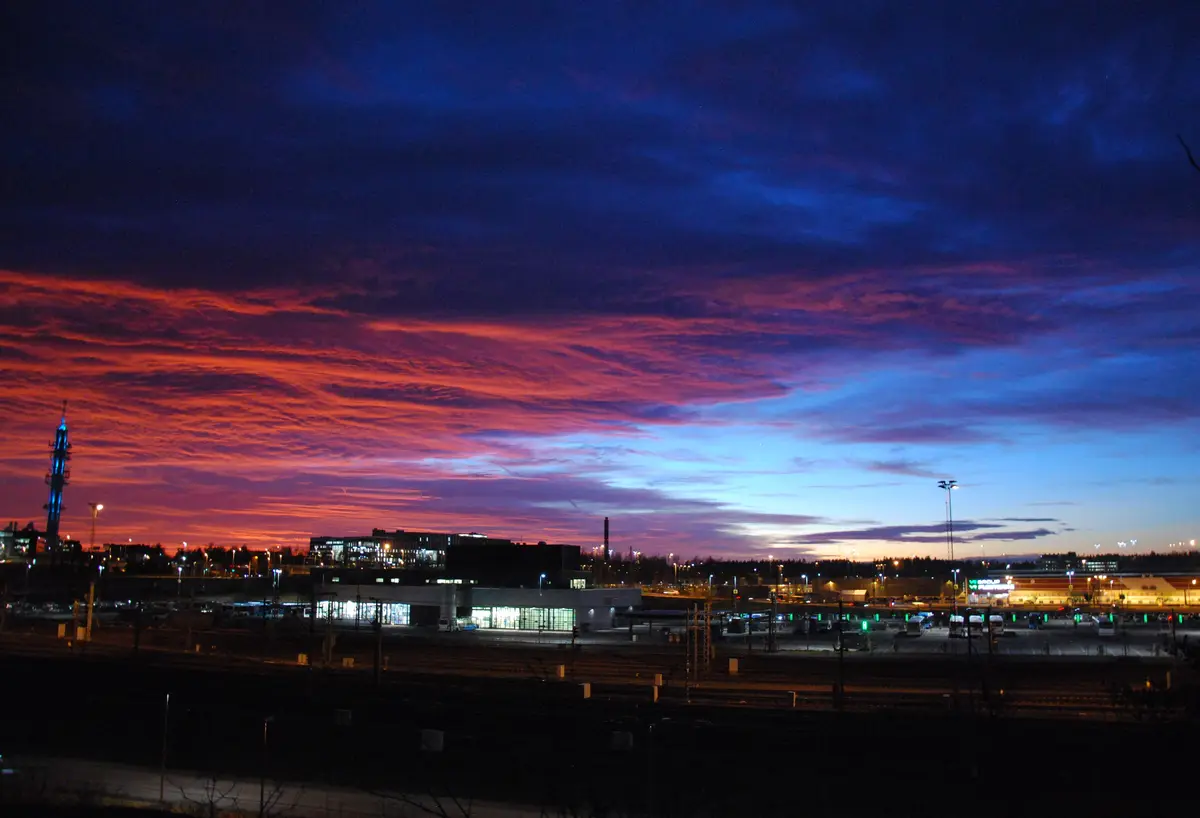 A photograph of a dramatic twilight sky over a cityscape, featuring vibrant orange and red clouds against a deep blue sky…