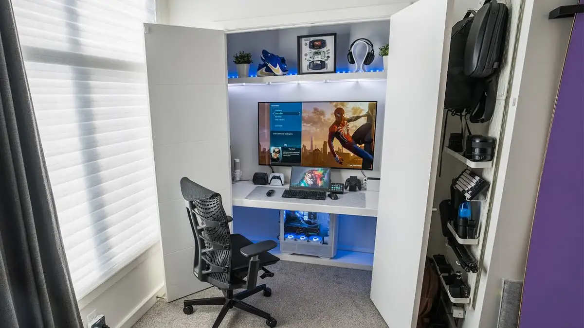 A neatly organized, white-walled gaming nook with a large monitor displaying a Spider-Man game, a gaming chair, and a custom…