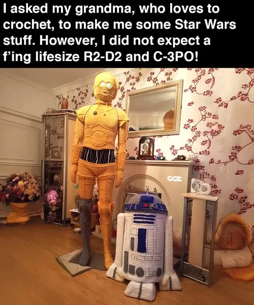 A room with floral wallpaper and wooden floors features two enormous, hand-crocheted Star Wars droids: a full-sized golden…
