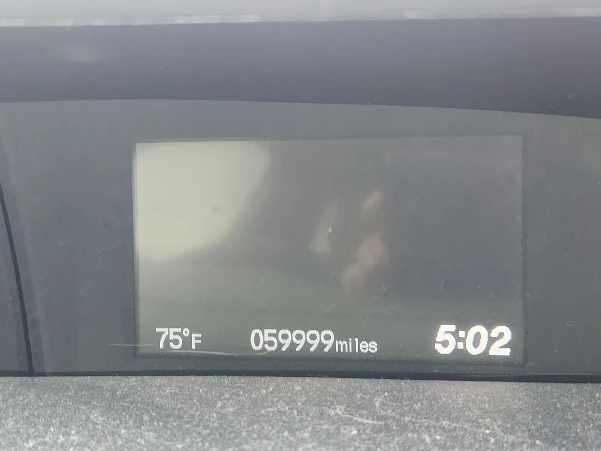 A close-up of a car's digital dashboard display showing 75°F temperature, 59999 miles, and 5:02 time, with a faint…