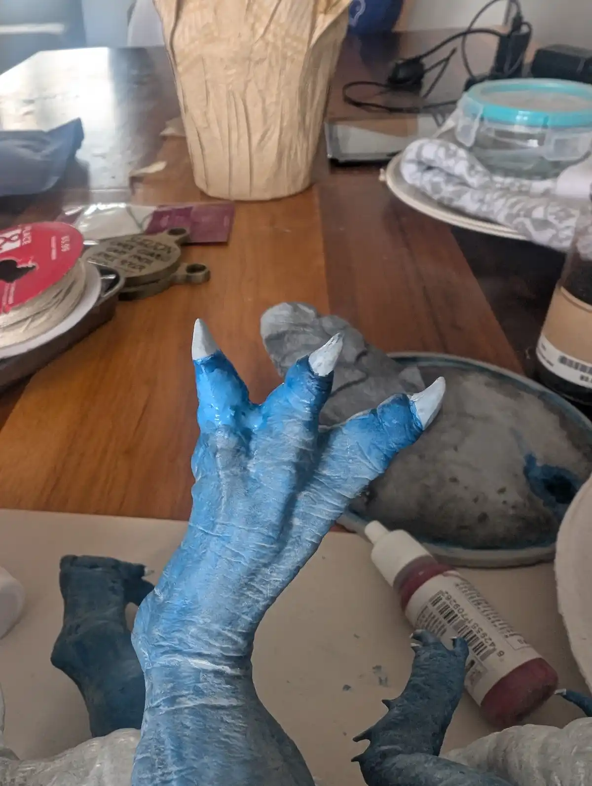 A close-up photo shows a person's hand painted blue with white claws, resembling a fantasy creature, held up over a…