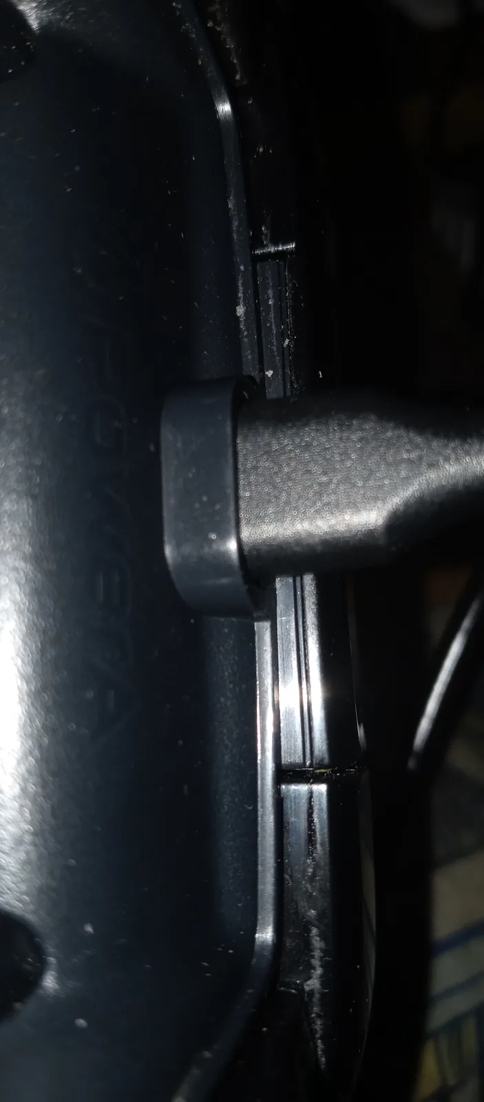 A close-up photo shows a black plastic hinge or latch mechanism on what appears to be a piece of equipment or appliance…