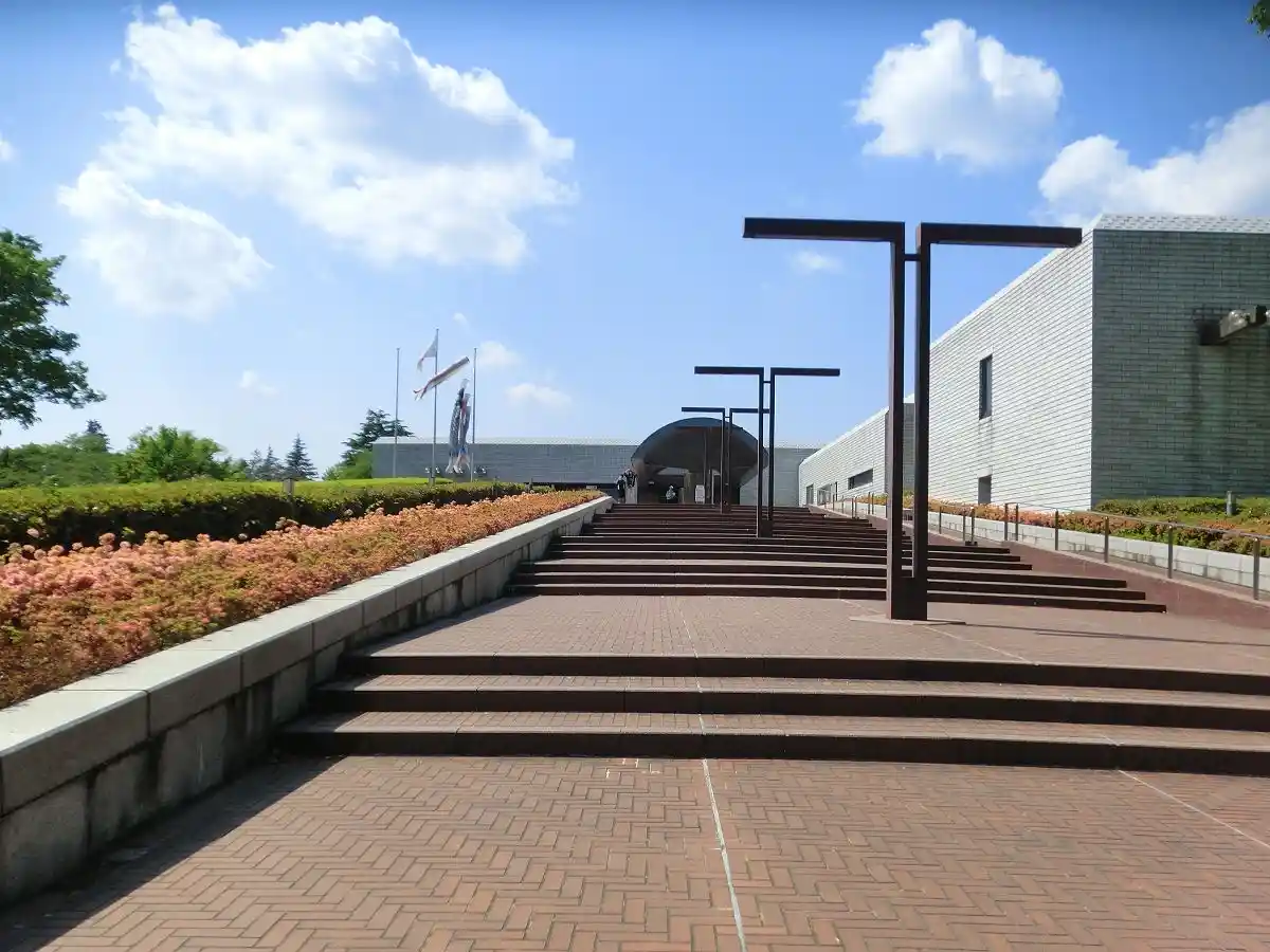 A wide-angle photo of a long, symmetrical staircase leading up to a modern building under a bright blue sky with fluffy…