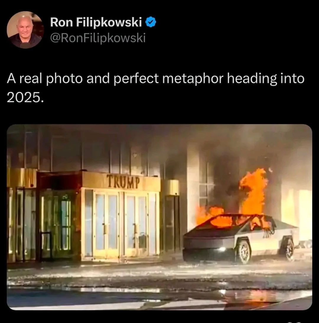 A nighttime photo shows a Tesla Cybertruck on fire, with flames engulfing its roof and sides, parked in front of a building…