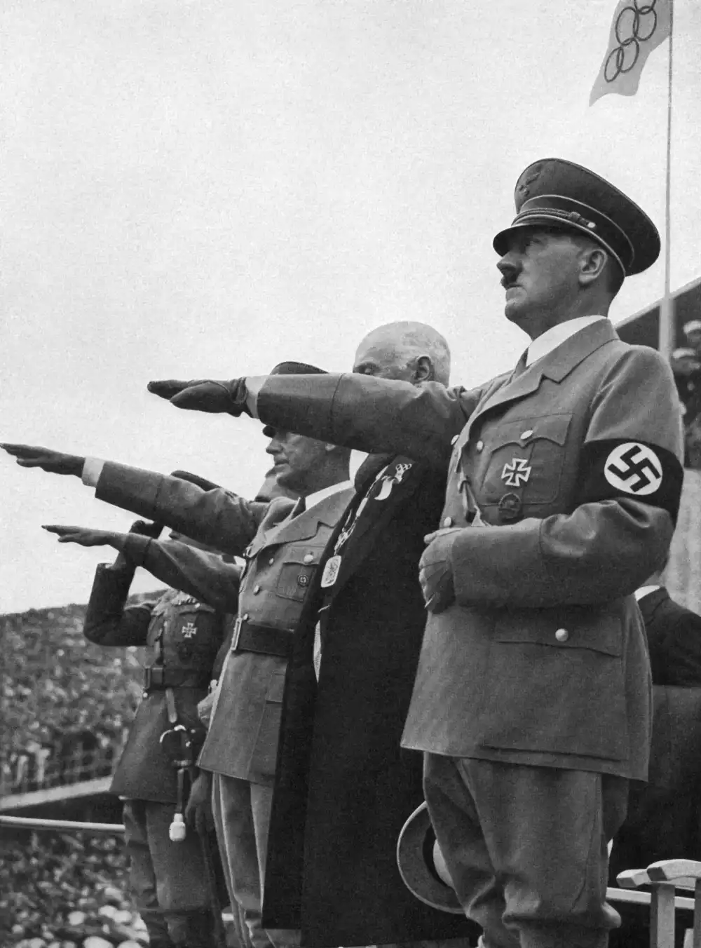 A black-and-white historical photograph shows Adolf Hitler and other Nazi officials performing the Nazi salute. Hitler is…