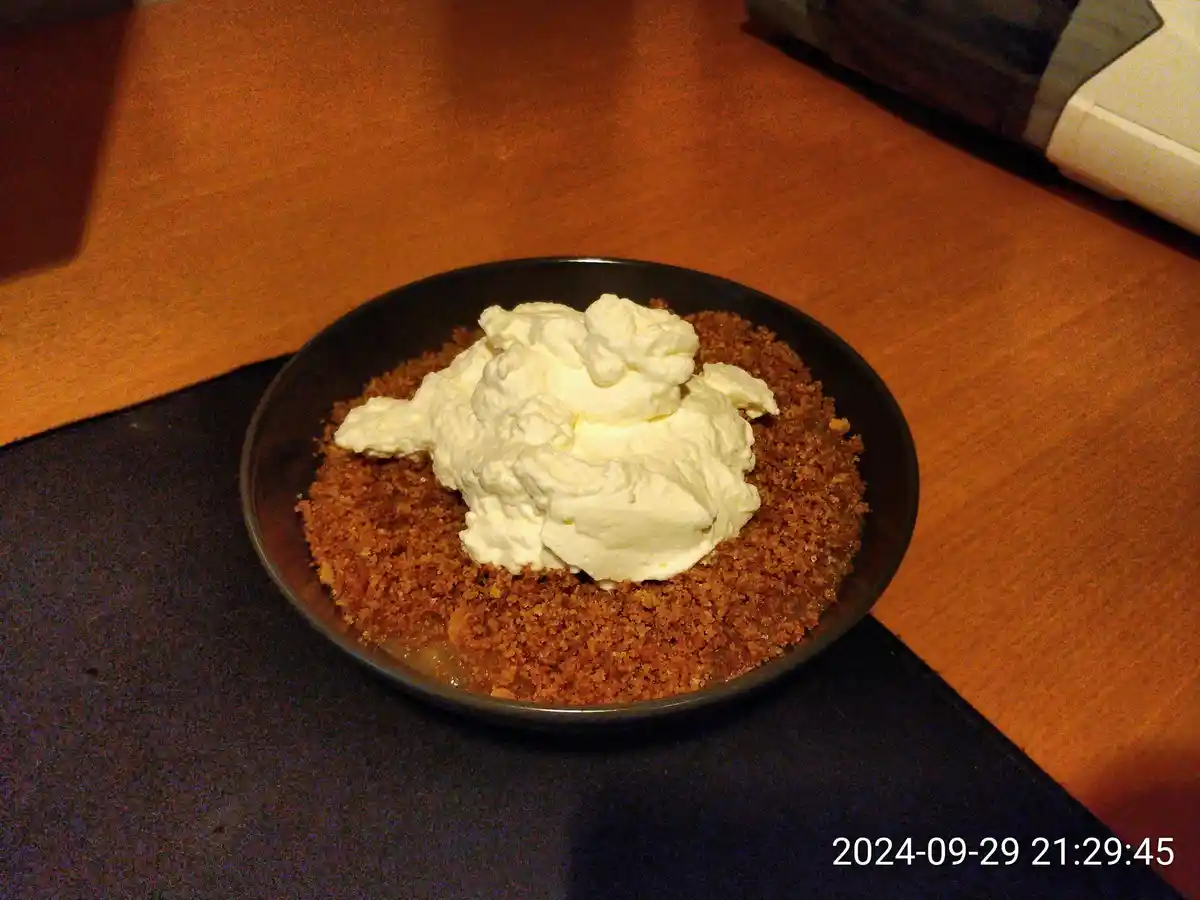 A close-up photo shows a black bowl filled with a dessert that appears to be a crumbly, brown base topped with a large…