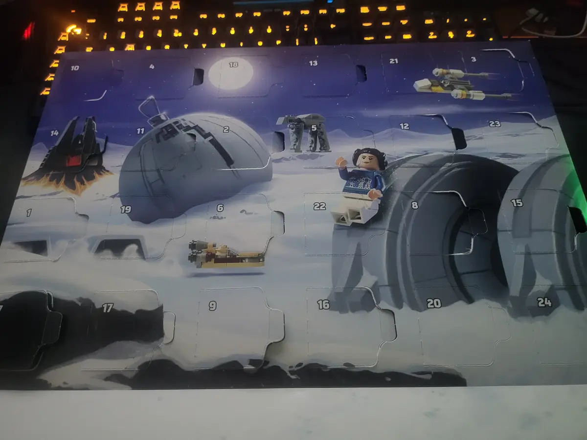 A Lego Star Wars Advent Calendar is shown with a Lego figure of Leia Organa sitting on a large tire, surrounded by various…