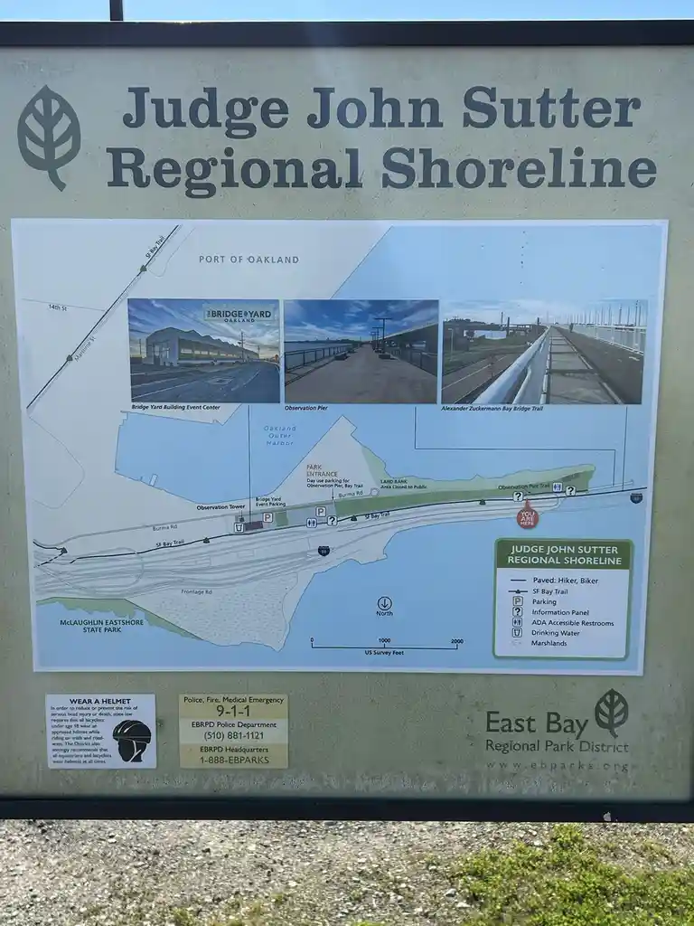 A public information sign for Judge John Sutter Regional Shoreline in Oakland, California, displays a map and photos of…