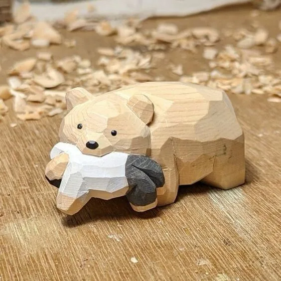 A hand-carved wooden bear figurine, with a geometric, faceted design, sits on a wooden workbench surrounded by wood…