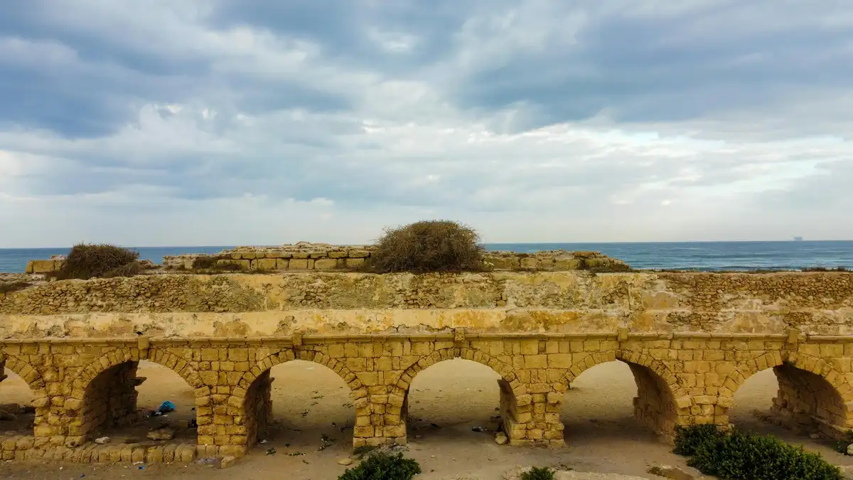 Ancient arches stretch across the landscape, worn smooth by time, as a fiery sky ablaze with oranges and yellows meets the…