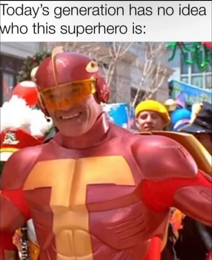 A person in a red and yellow superhero costume with a large 'T' on the chest and orange goggles smiles confidently at the…