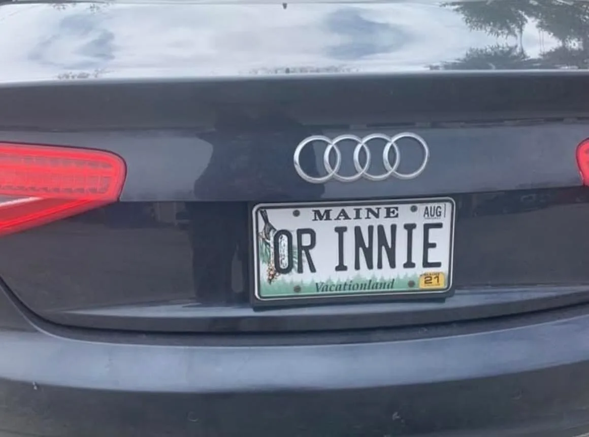 The image shows the rear of a black Audi car with a Maine license plate that reads 'OR INNIE'. The plate includes the state…