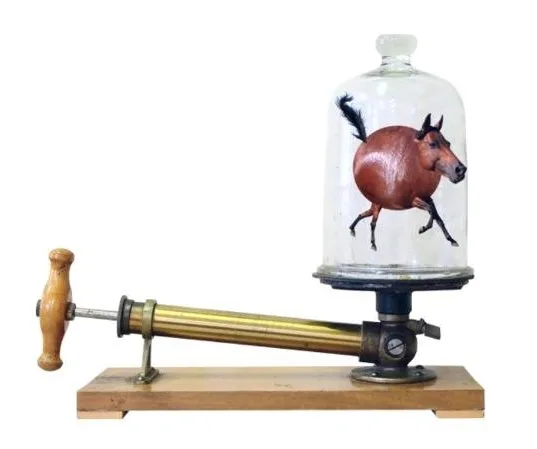 A vintage-style vacuum pump with a wooden handle and brass cylinder is mounted on a wooden base, connected to a glass bell…