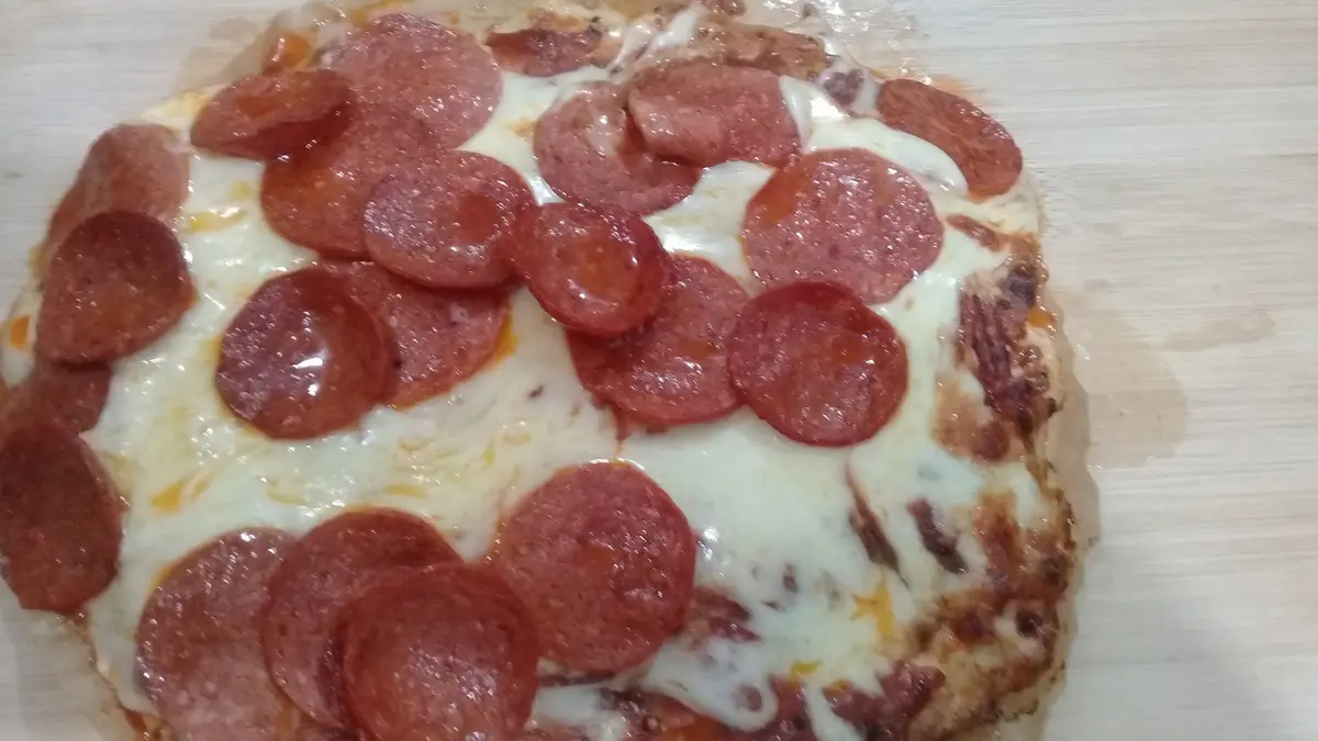 A close-up photo of a pepperoni pizza with melted cheese and slightly burnt crust on a wooden surface. The overlaid text…
