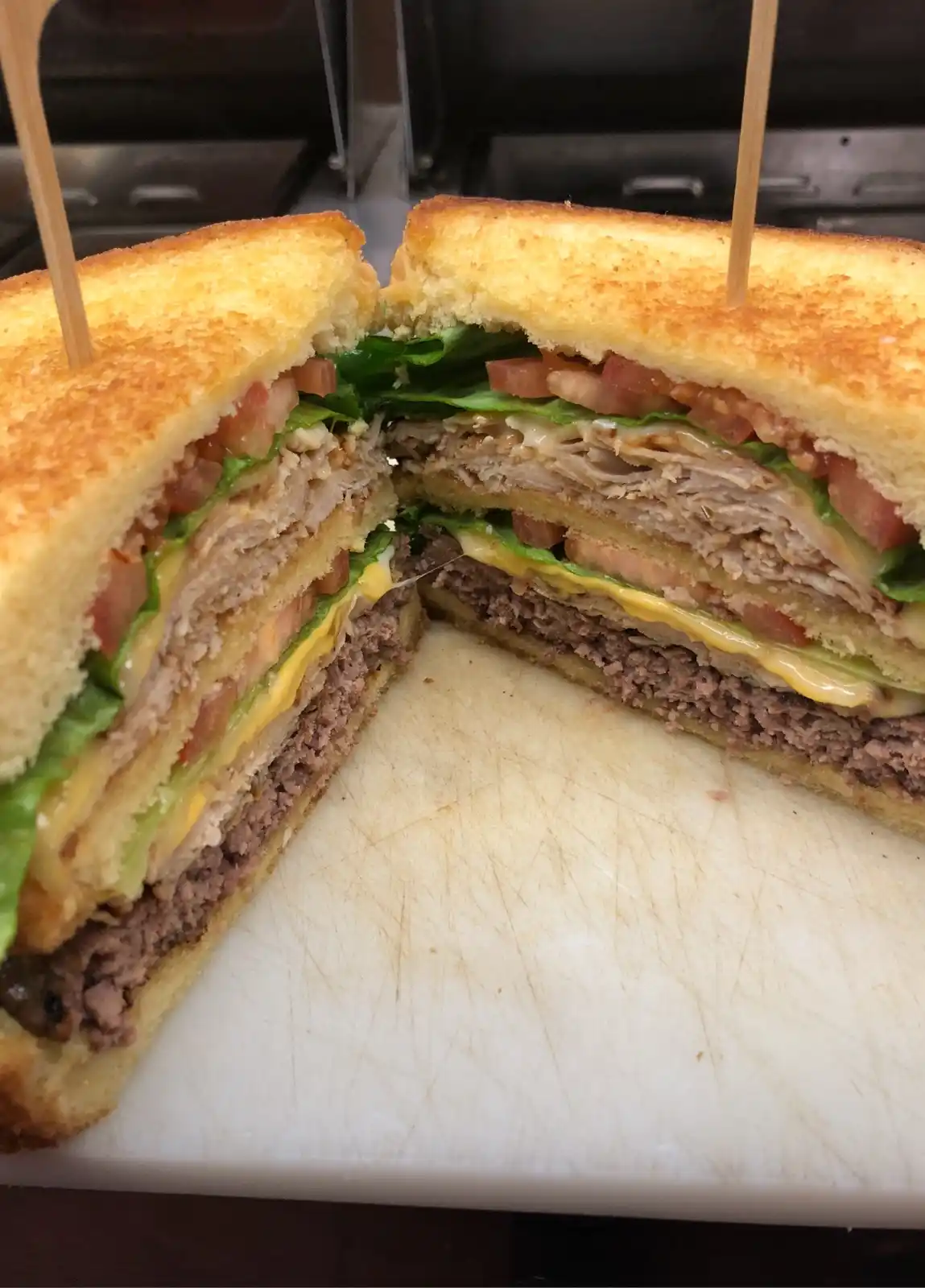 A close-up photo shows a large, toasted sandwich cut in half, held together by wooden skewers, revealing multiple layers…