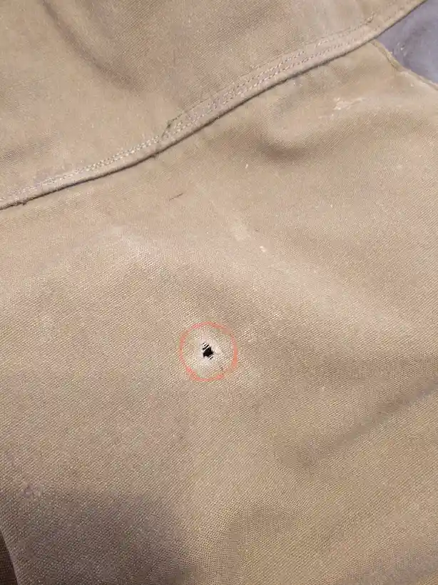 A close-up photo shows a small, torn hole in a beige fabric garment, likely pants, with a red circle drawn around it to…