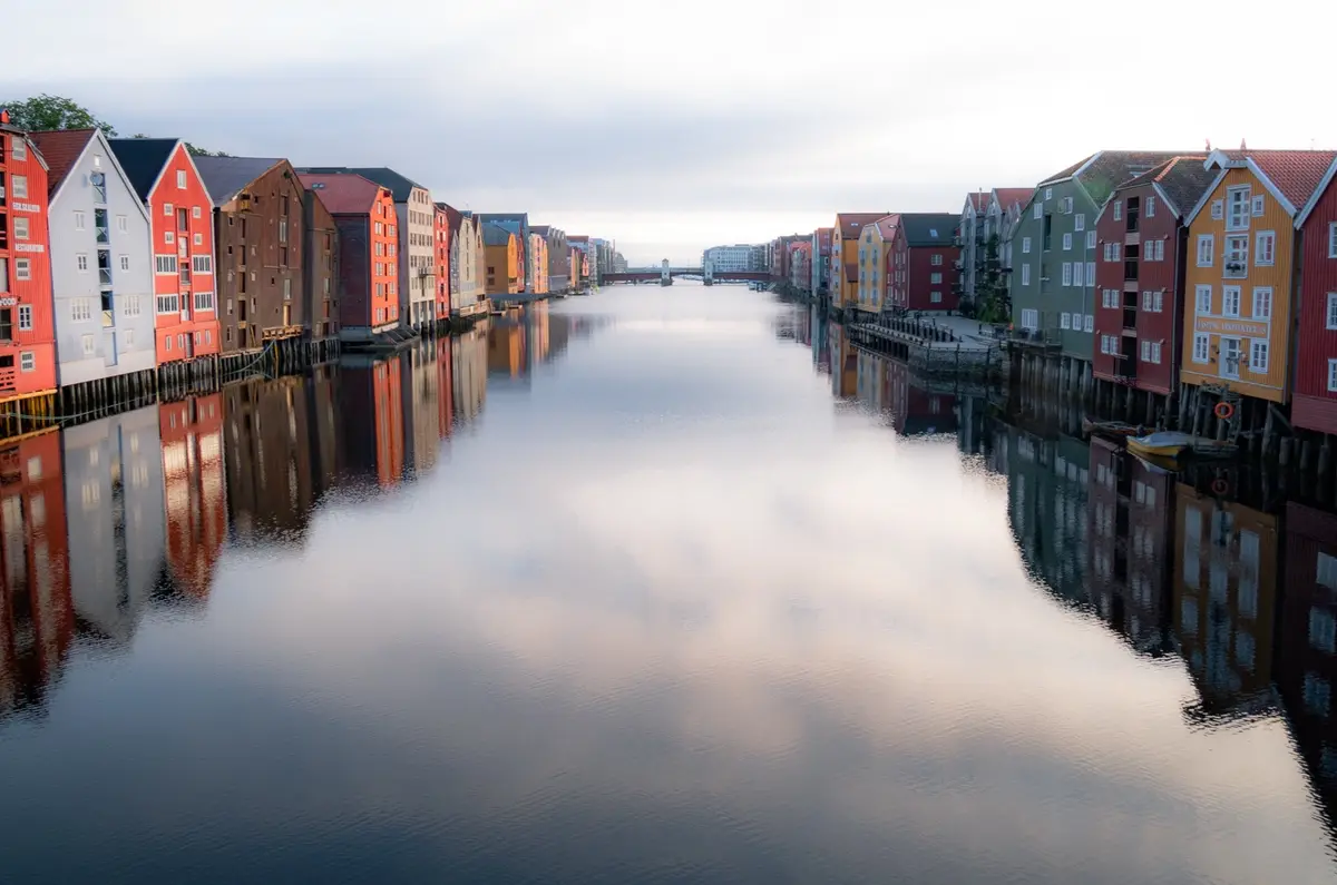 A serene photo of colorful wooden buildings lining a calm canal, their reflections mirrored perfectly in the water under an…