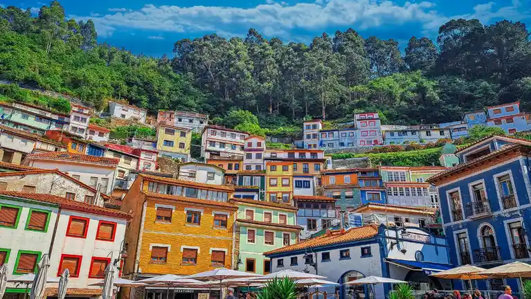 A vibrant, heavily saturated photo of colorful, densely packed houses cascading up a green hillside under a bright blue sky…