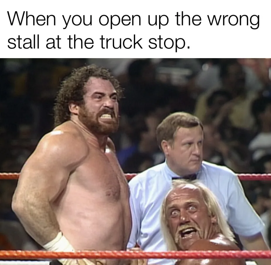 A shirtless, muscular wrestler with curly hair and a beard stands in a wrestling ring, glaring intensely with bared teeth…