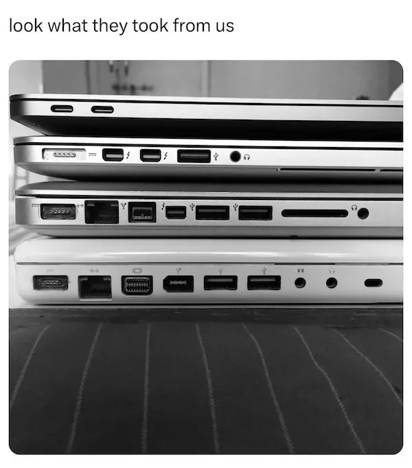 A black-and-white photo shows four laptops stacked vertically, displaying their ports. The top laptop has minimal ports…