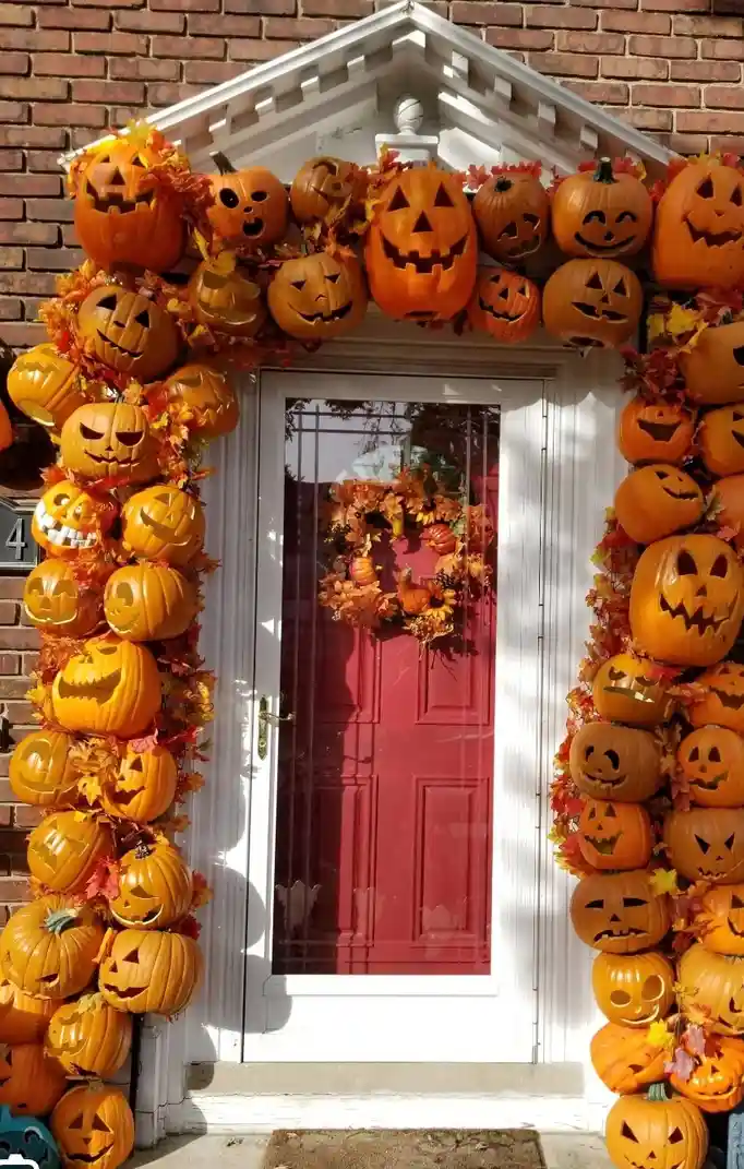 A front door is framed by an excessive and dense arrangement of carved jack-o'-lanterns and autumn leaves, creating a…