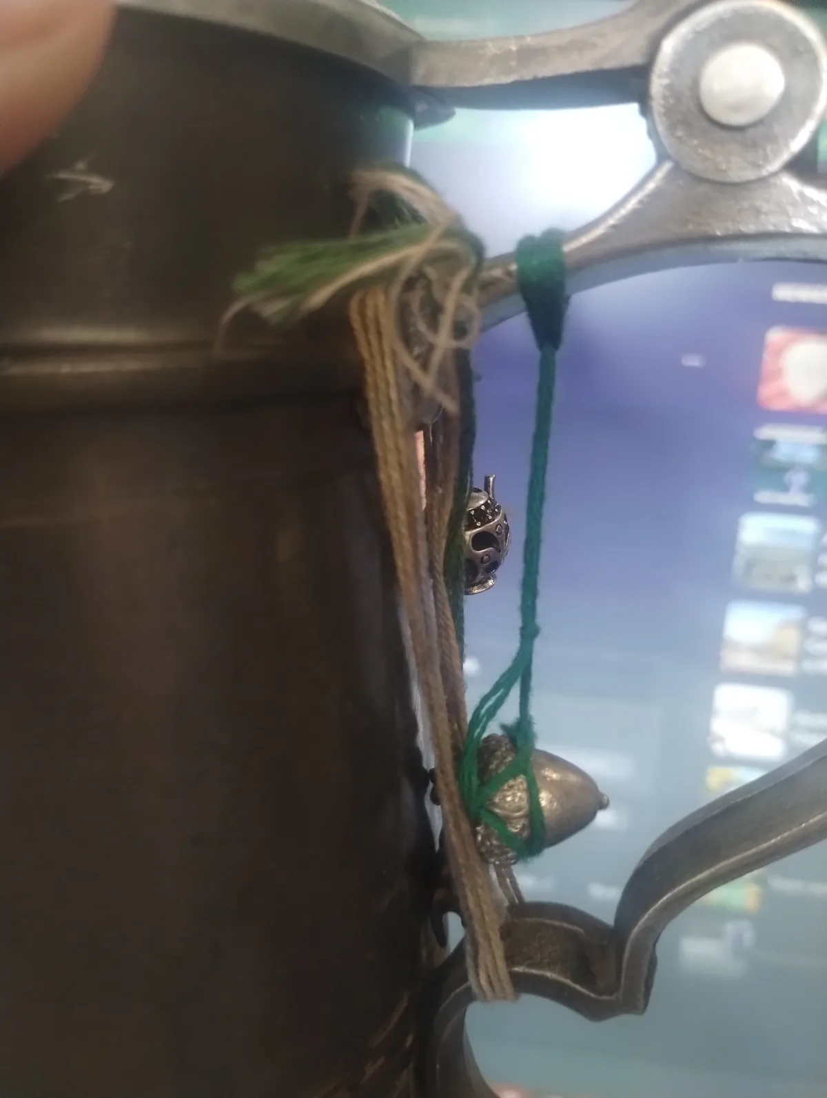 A close-up photo shows a dark metal trophy with a handle, adorned with green and beige strings tied around it, holding small…